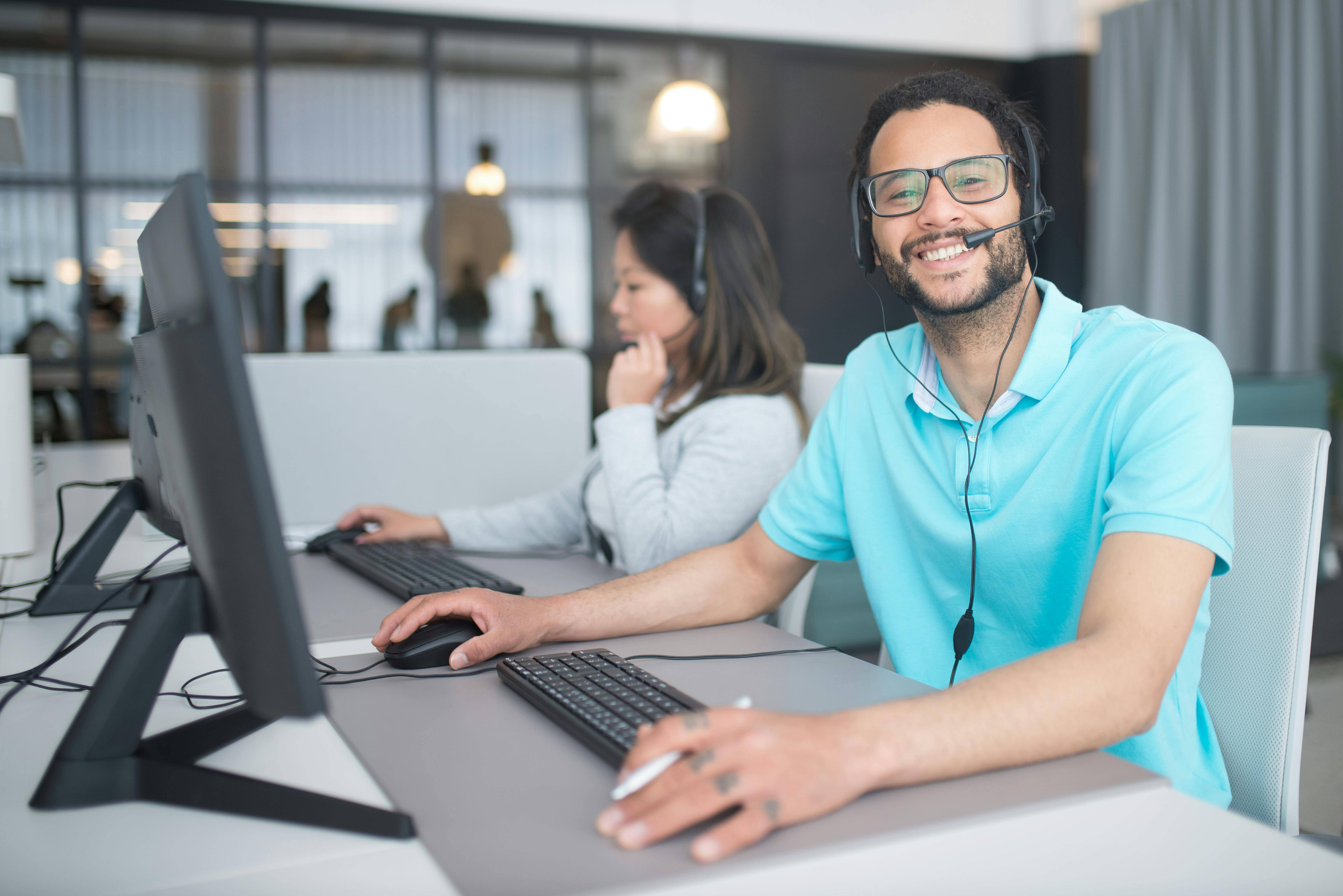 Smiling call center team member with headset on, seated at his desks, looking towards the camera