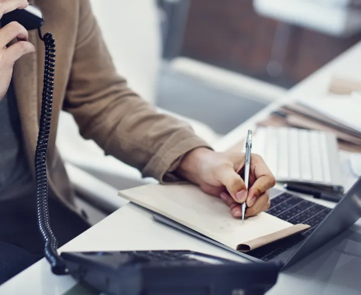 close up writing notes while using office phone system