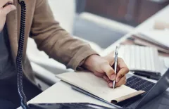 close up writing notes while using office phone system